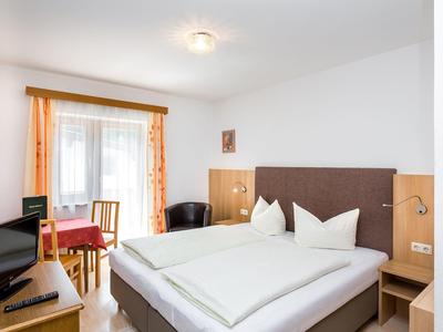 Bright hotel room with double bed, TV, table, and chairs near window with curtains.