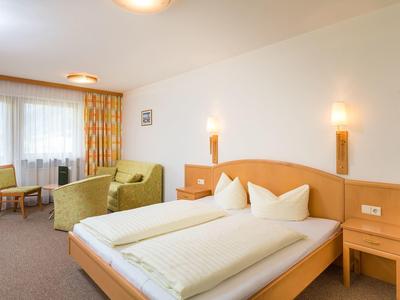Bright hotel room with double bed, two armchairs, and a small table by window with curtains.