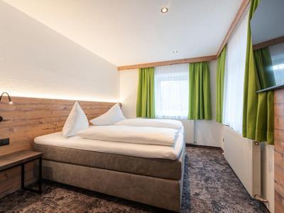 Modern hotel room with double bed, green curtains, and wall-mounted TV.