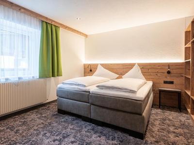 Modern hotel room with cozy double bed, wood paneling, and green curtain at the window.