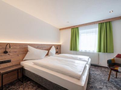 Cozy hotel room with large double bed, wooden headboard, and green curtains at the window.