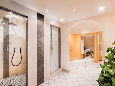 Modern hotel shower with glass partition and light tiles in hallway next to green plant