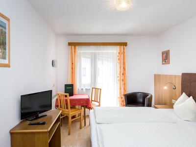 Bright hotel room with two single beds, TV, table with chairs, and balcony with curtains.