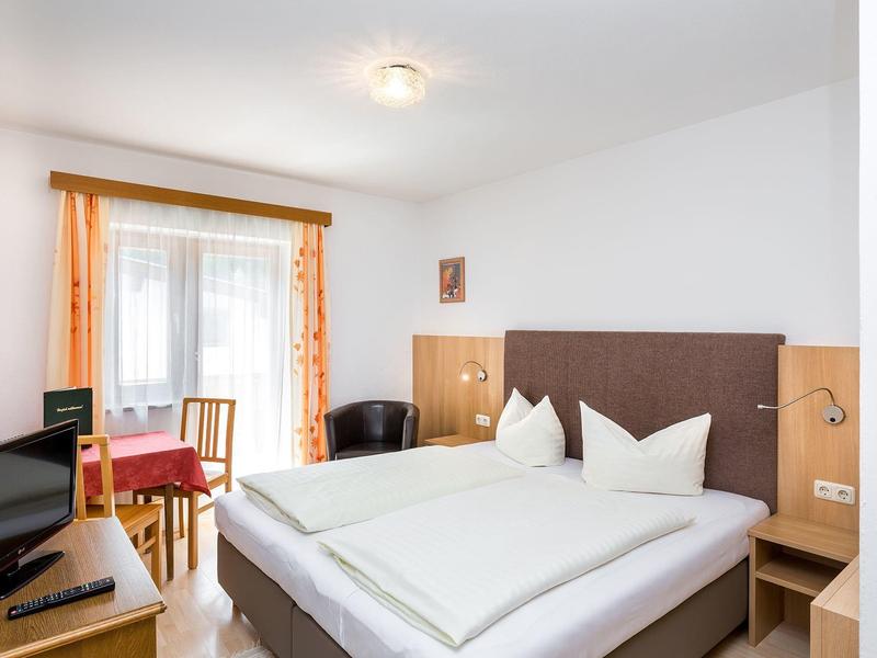 Bright hotel room with double bed, TV, table, and chairs near window with curtains.