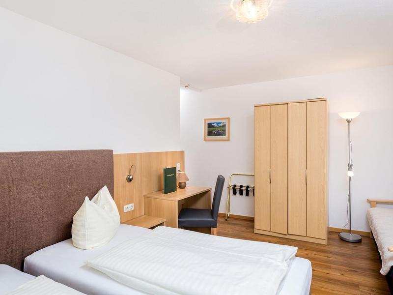 Hotel room with two beds, a wardrobe, desk, and chair, bright and simply furnished.