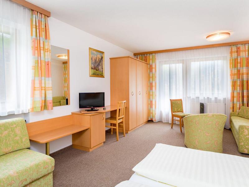 Brightly furnished hotel room with seating area, desk, and large windows with curtains.