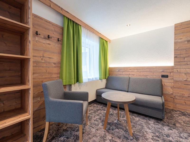 Cozy seating area with gray sofa, armchair, wooden table, and green curtains by a window.