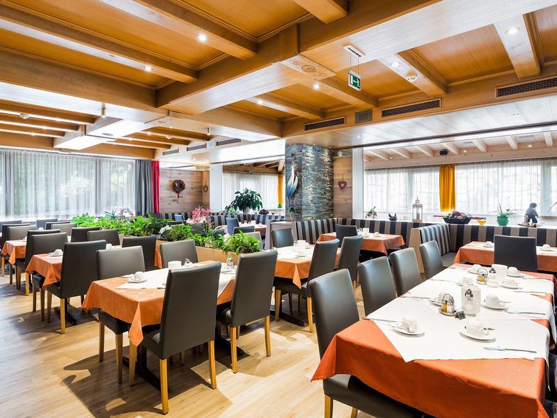 Spacious hotel restaurant with set tables and modern wooden ceiling beams.