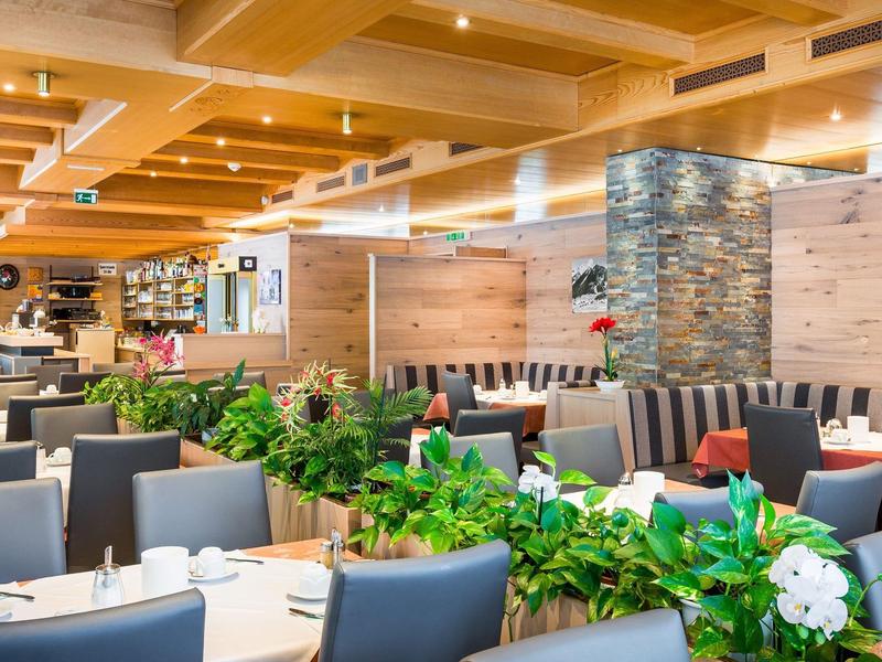 Bright, modern restaurant with wooden beam ceiling and green plants as space dividers.