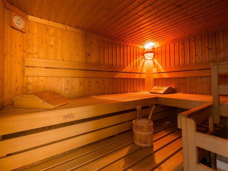 Cozy sauna with wooden benches, wood-paneled walls, and a bucket under the lamp.