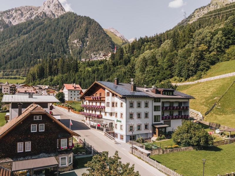 Alpine hotel buildings in a green valley with mountains in the background under clear weather.