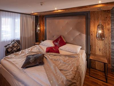 Gemütliches Hotelzimmer mit großem Bett, dekorativen Kissen und warmem Holzinterieur.