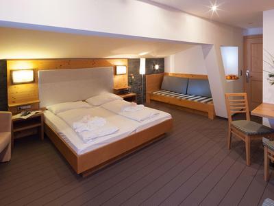 Helles Hotelzimmer mit Doppelbett, Sofa, Tisch und Stühlen in modernem Design.