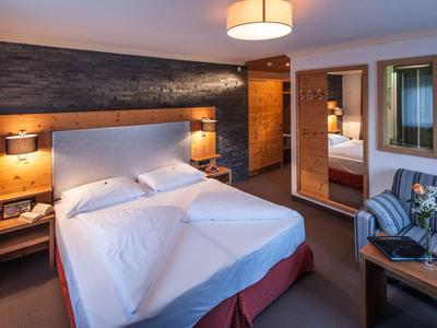 Modern eingerichtetes Hotelzimmer mit großem Bett, zwei Nachttischen und Sitzbereich mit Tisch.