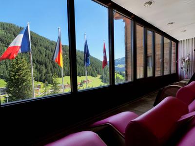 Blick aus einem Hotelzimmer mit roten Sesseln auf mehrere Flaggen vor einem bewaldeten Berg.