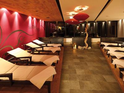 Innenraum eines Spa-Bereichs mit Liegen, warmem Licht und dekorativer Wand in Rot.