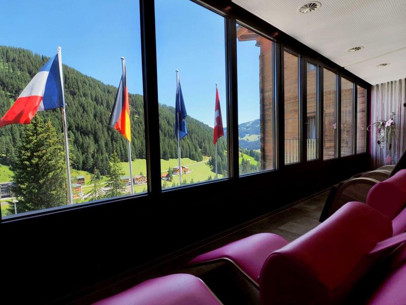 Blick aus einem Hotelzimmer mit Sitzbereich auf Berge und Flaggen im Außenbereich.