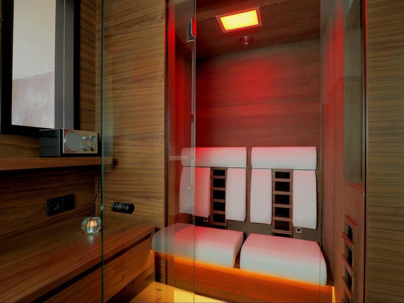 Moderne Sauna mit Holzwänden, roten Lichtakzenten und weißen gepolsterten Sitzen.