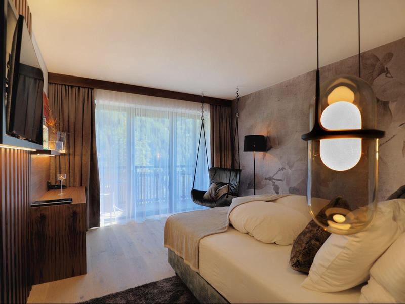 Modernes Hotelzimmer mit Bett, Schreibtisch, Fernseher und großem Fenster mit Vorhängen.