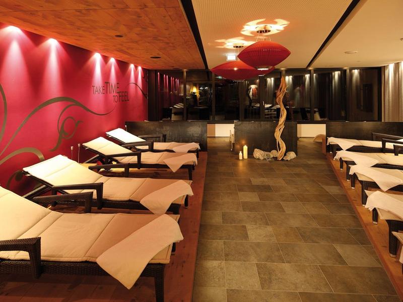 Innenraum eines Spa-Bereichs mit Liegen, warmem Licht und dekorativer Wand in Rot.