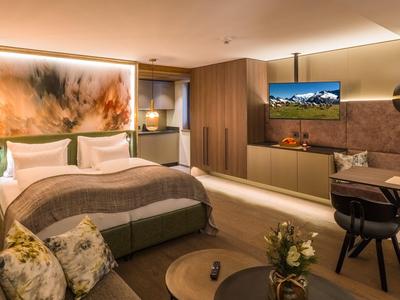 Modern eingerichtetes Hotelzimmer mit Doppelbett, Couch und Fernseher an der Wand.