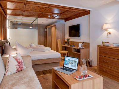 Modernes Hotelzimmer mit Doppelbett, Couch, TV, Schreibtisch und Holzdecke.