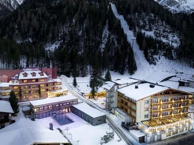 Verschneites Hotelresort in einem Bergtal mit beleuchteten Gebäuden und Wald im Hintergrund.