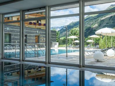 Moderner Innenpool mit Glaswänden, Blick auf Außenpool und Berge bei sonnigem Wetter.
