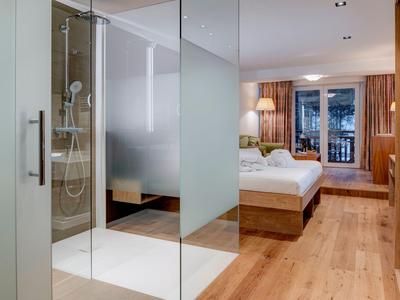 Modernes Hotelzimmer mit Holzboden, großem Bett und gläserner Dusche.