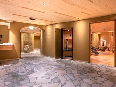 Ein heller Hotelkorridor mit Natursteinboden und offenen Türen zu gemütlichen Aufenthaltsräumen.