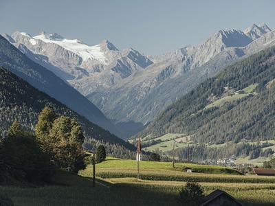 Schneebedeckte Berge und grüne Täler mit Häusern unter klarem Himmel.