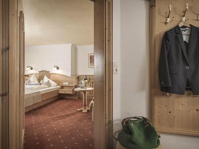 Blick durch eine Tür auf ein gemütliches Hotelzimmer mit Bett, Tisch und Stuhl.