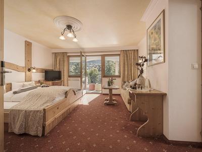 Helles Hotelzimmer mit Doppelbett, Fernseher, Schreibtisch und Balkon mit Blick ins Grüne.