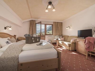 Helles Hotelzimmer mit zwei Betten, einem Fernseher und Blick auf Berge durch das Fenster.