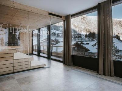 Moderne Hotel-Sauna mit großen Fenstern und Blick auf verschneite Berge und Gebäude.