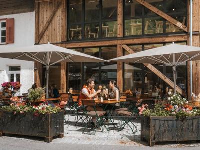 Gemütliche Außenterrasse eines Hotels mit Gästen, die unter Sonnenschirmen an Tischen sitzen.