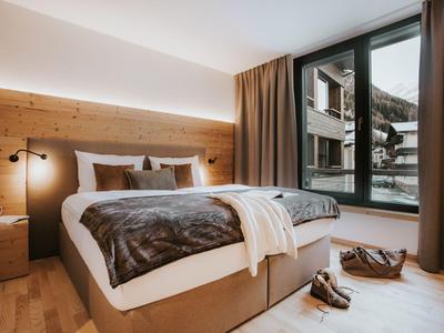 Modernes Hotelzimmer mit großem Bett, Holzwand und Fenstern mit Bergblick.
