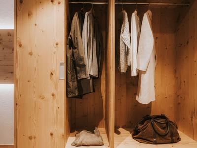 Ein offener Holzkleiderschrank mit hängenden Kleidungsstücken und Taschen im unteren Fach.
