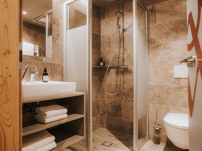 Modernes Badezimmer mit Dusche, Waschbecken, Toilette und Handtüchern in warmer Holzeinrichtung.