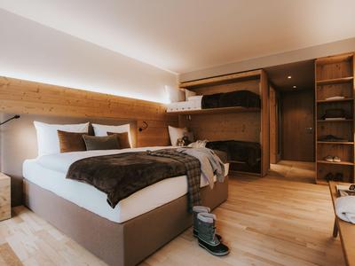 Modernes Hotelzimmer mit Doppelbett, Etagenbett, Holzboden und gemütlicher Beleuchtung.