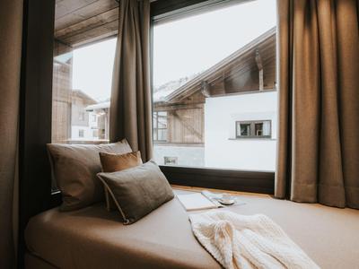 Gemütliche Sitzbank mit Kissen vor Fenster mit Blick auf Chaletdach.