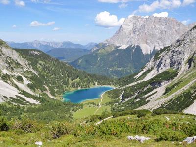 Berglandschaft mit einem klaren blauen See, umgeben von Felsen und grüner Vegetation unter blauem Himmel.