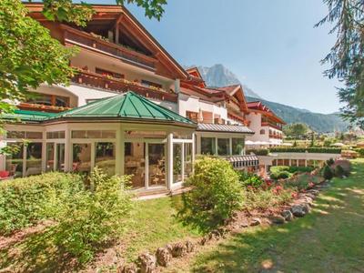 Luxuriöses Hotel mit Holzfassade, Wintergarten und gepflegtem Garten in bergiger Umgebung.