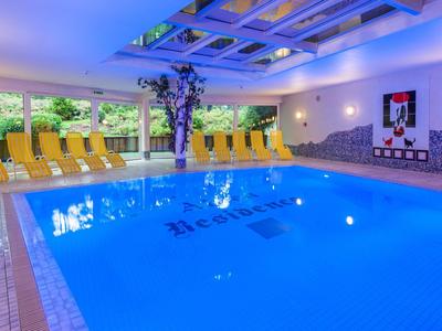 Innenhotel mit beleuchtetem Schwimmbad und gelben Liegestühlen neben großen Fenstern.