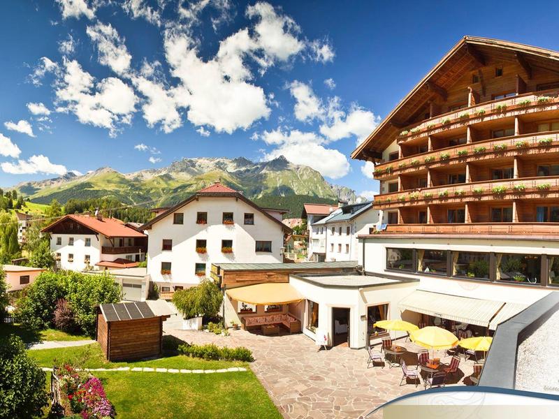 Bergdorf mit traditionellen Holzhäusern, grünem Garten und bewölktem, blauem Himmel.