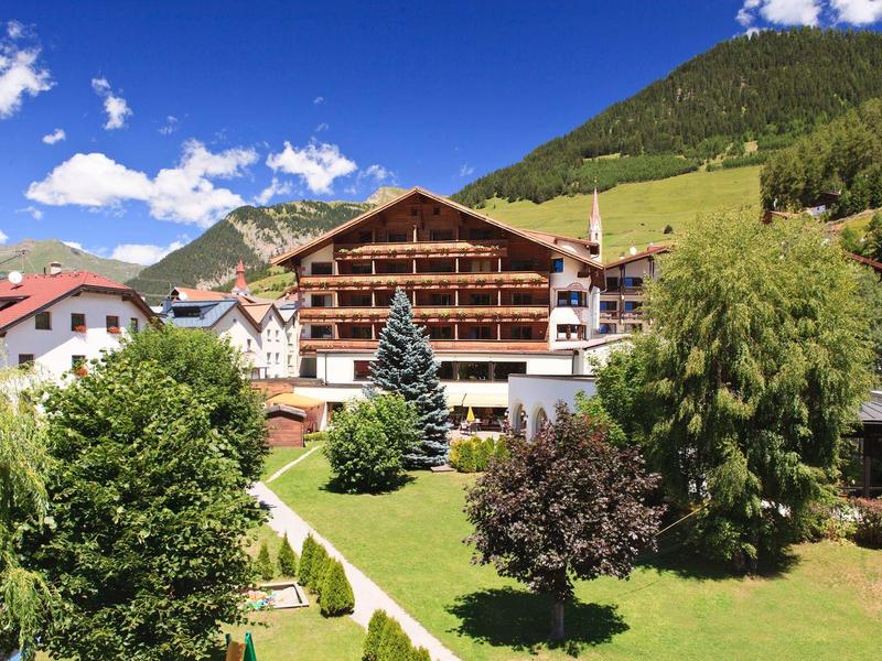 Hotelgebäude in den Bergen mit einem gepflegten Garten und Rasen im Vordergrund.