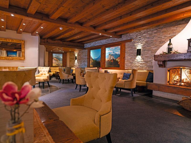 Gemütliches Wohnzimmer mit Holzdecke, gelben Sesseln und brennendem Kamin hinter Steinwand.