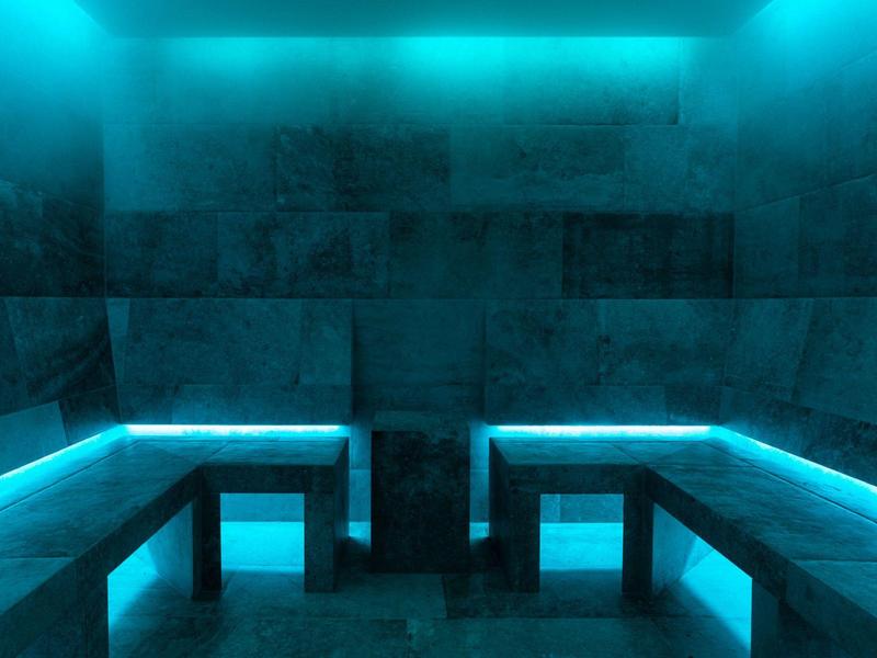 Dunkler Raum mit blauer LED-Beleuchtung und drei grauen Steinbänken an den Wänden.