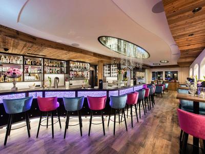 Moderner Hotelbarbereich mit bunten Barhockern und Holzdecke in warmem Ambiente.