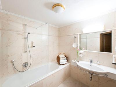 Helles Badezimmer mit beiger Fliesenwanne, Glasbadewannenabtrennung und großem Spiegel über dem Waschbecken.